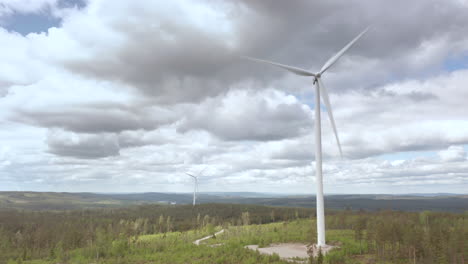 Wide-aerial-of-wind-turbines-spinning-in-forested-landscape-on-overcast-day