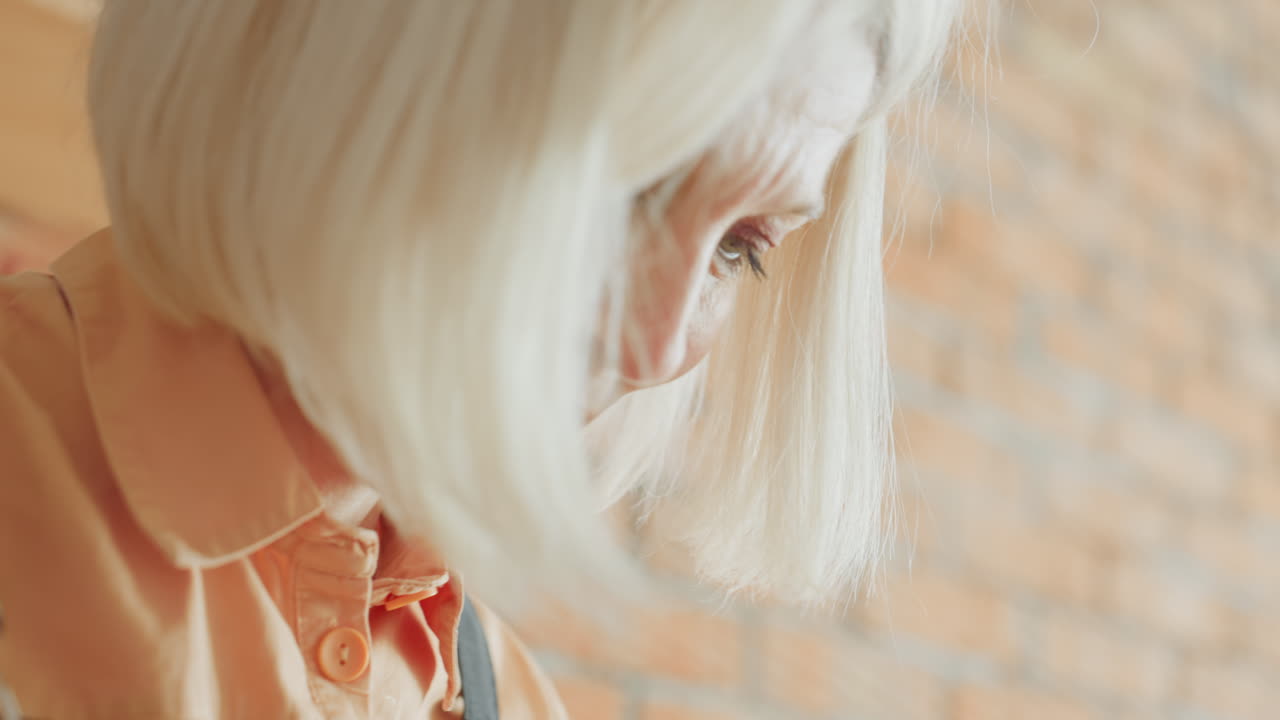 Close up of female hands holding handmade floral wreath made of twigs, hay, and artificial flowers against brick wall background, showing craftsmanship and natural rustic decorative design in progress