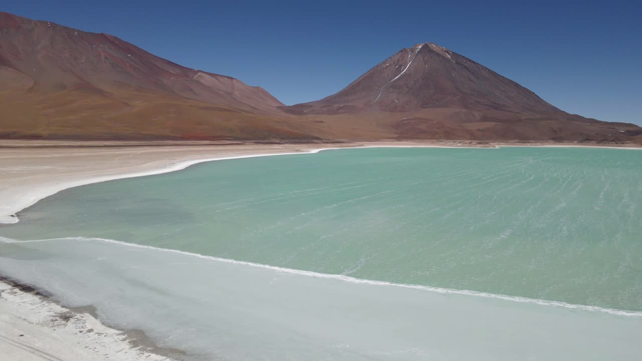 Aerial approach to Laguna Verde in Bolivia with dramatic volcanic mountain rising behind it