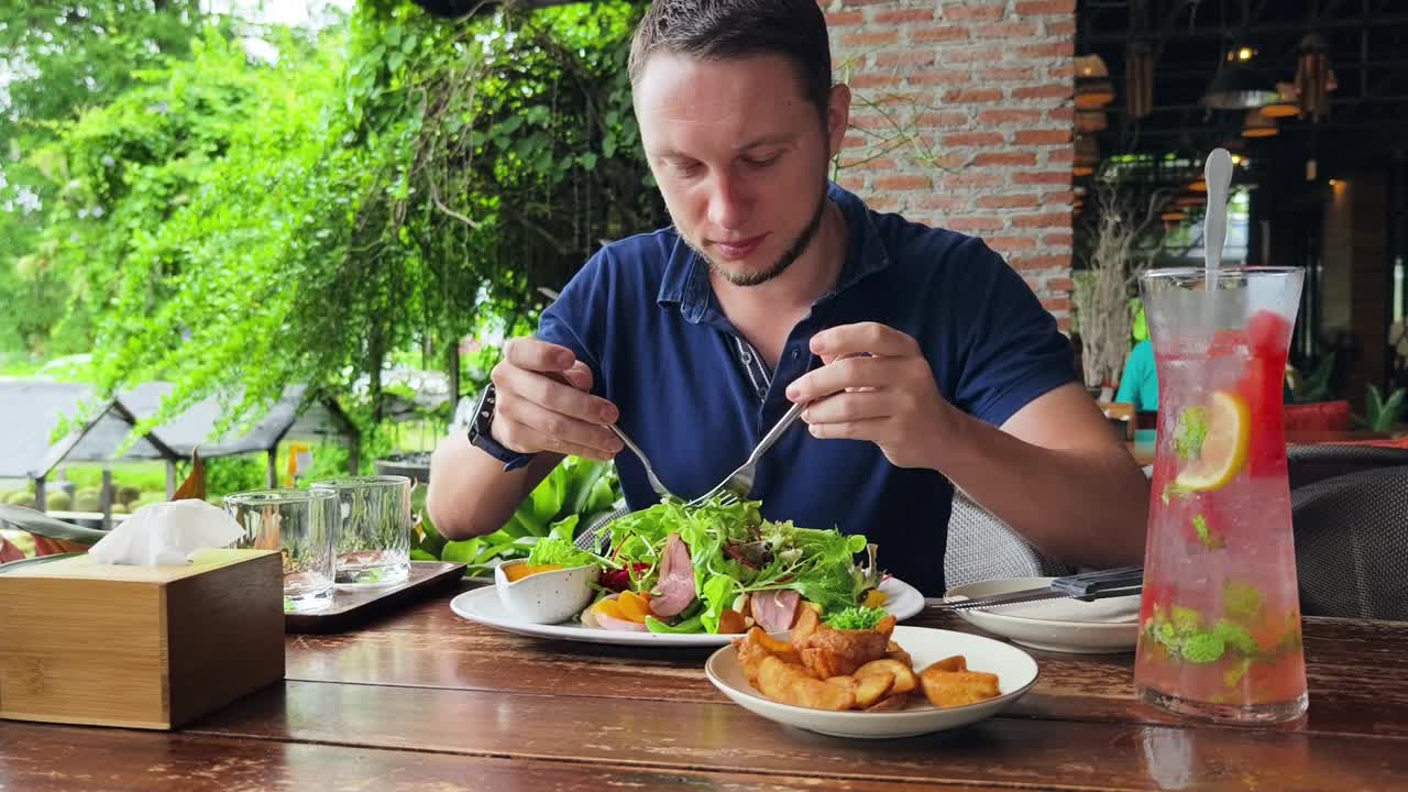 hombre disfrutando de una comida con ensalada, pato y papas fritas en un café al aire libre