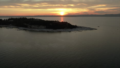 revelación aérea de una franja de tierra en el medio del lago sirmione con una impresionante puesta de sol y paisaje de nubes en el fondo