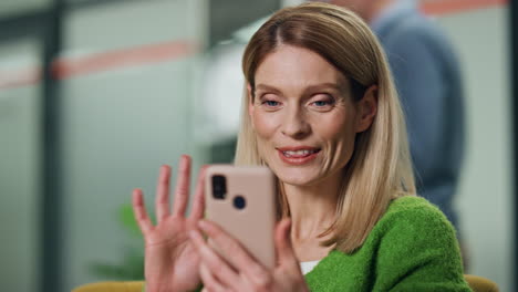 happy ceo video chatting smartphone workplace closeup. business woman greeting