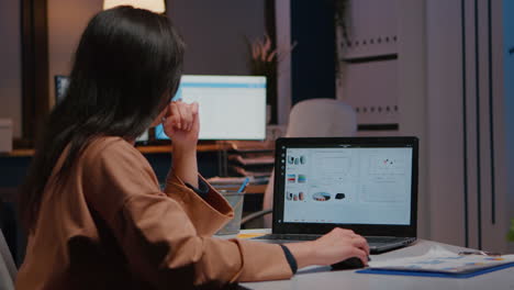 overworked businesswoman typing financial statistics on laptop sitting at desk