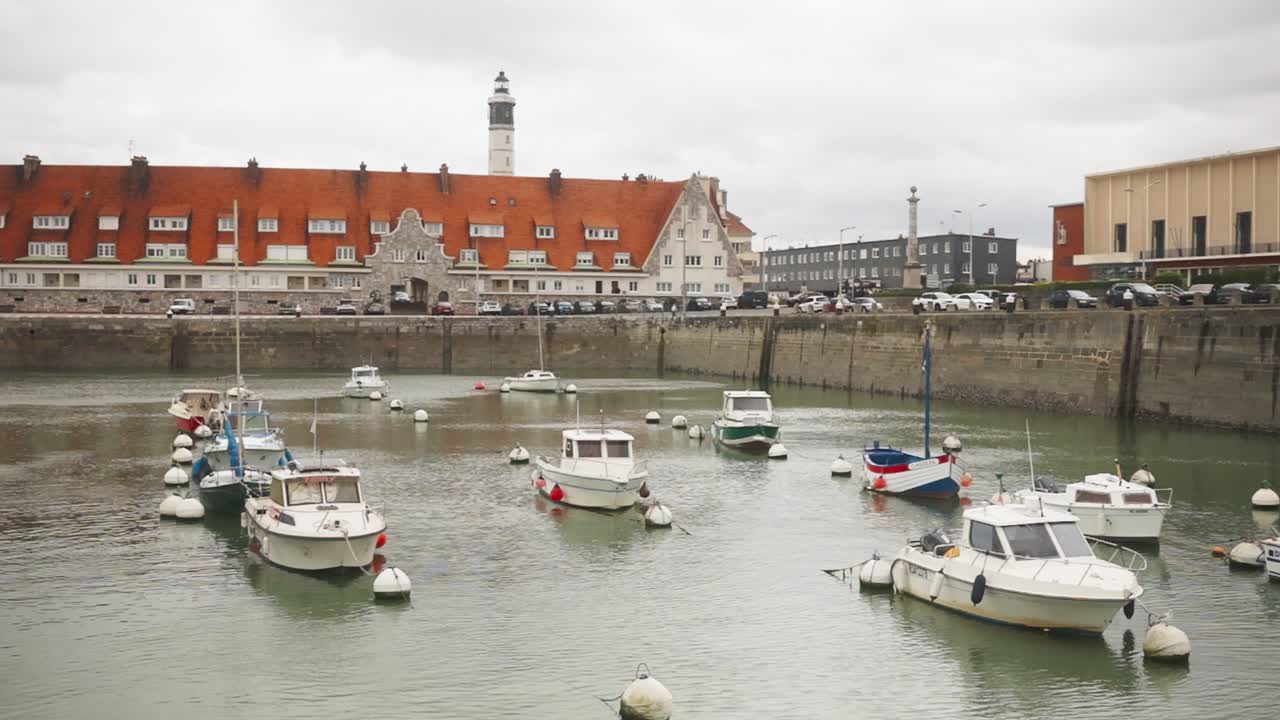 Fishing boats moored in Calais harbor with historic buildings and lighthouse in the background