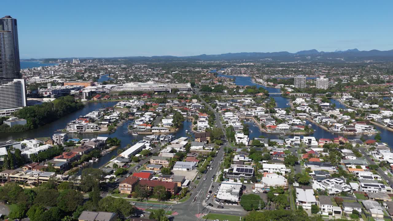 Drone footage captures a sunny, expansive view of a coastal city with rivers, buildings, and distant mountains