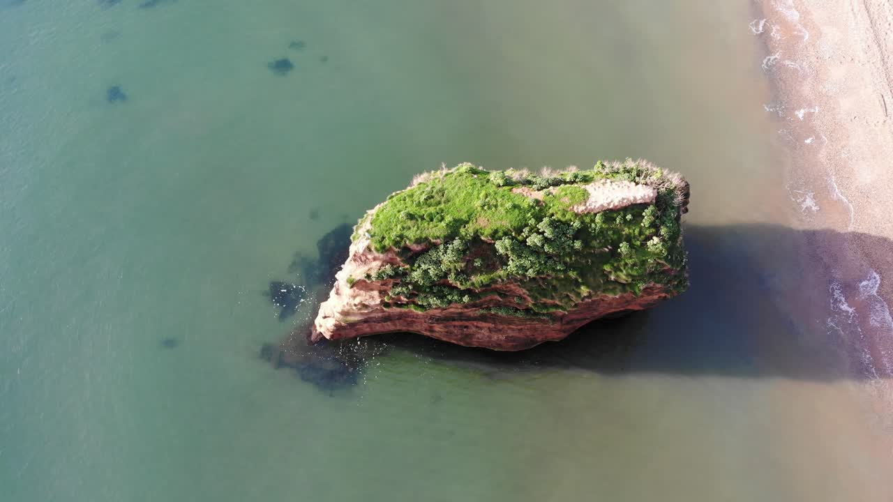 hermosa y exuberante vegetación pura cubre el majestuoso pilar de roca en la costa de la tranquila bahía de ladram