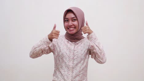 carefree young asian muslim girl standing while presenting both sides and showing thumbs up