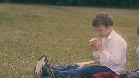 boy-with-fair-hair-eats-sandwich-sitting-on-green-grass