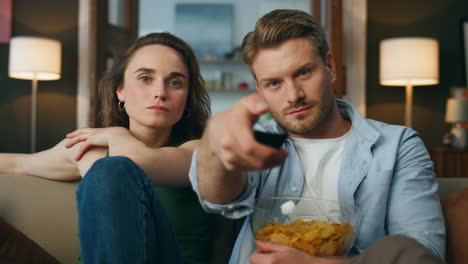 una pareja feliz sentada en el sofá viendo la televisión en casa. un hombre barbudo cambia de canal.
