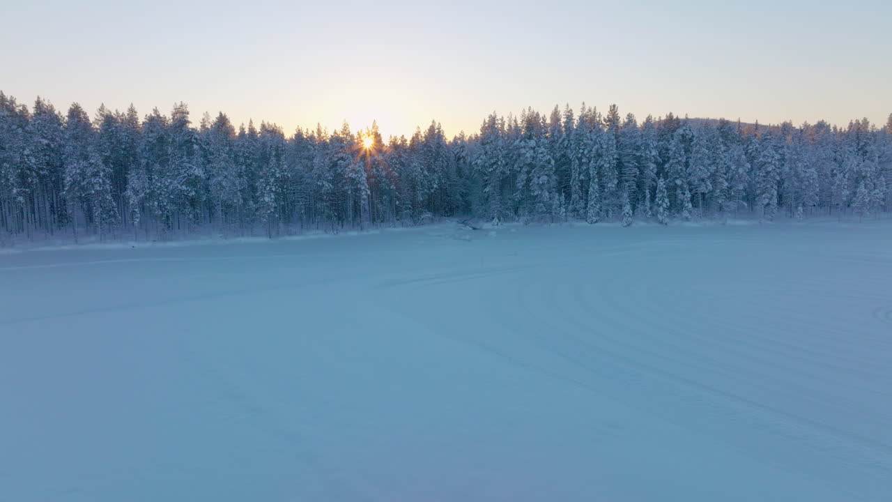 Flyfoto av Norrbotten svensk Lappland Polarsirkelen, med strålende gyllen soloppgang som skinner gjennom snødekt skog og islagt innsjø