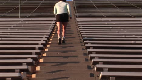 crab-left of a woman run up the steps of a large stadium