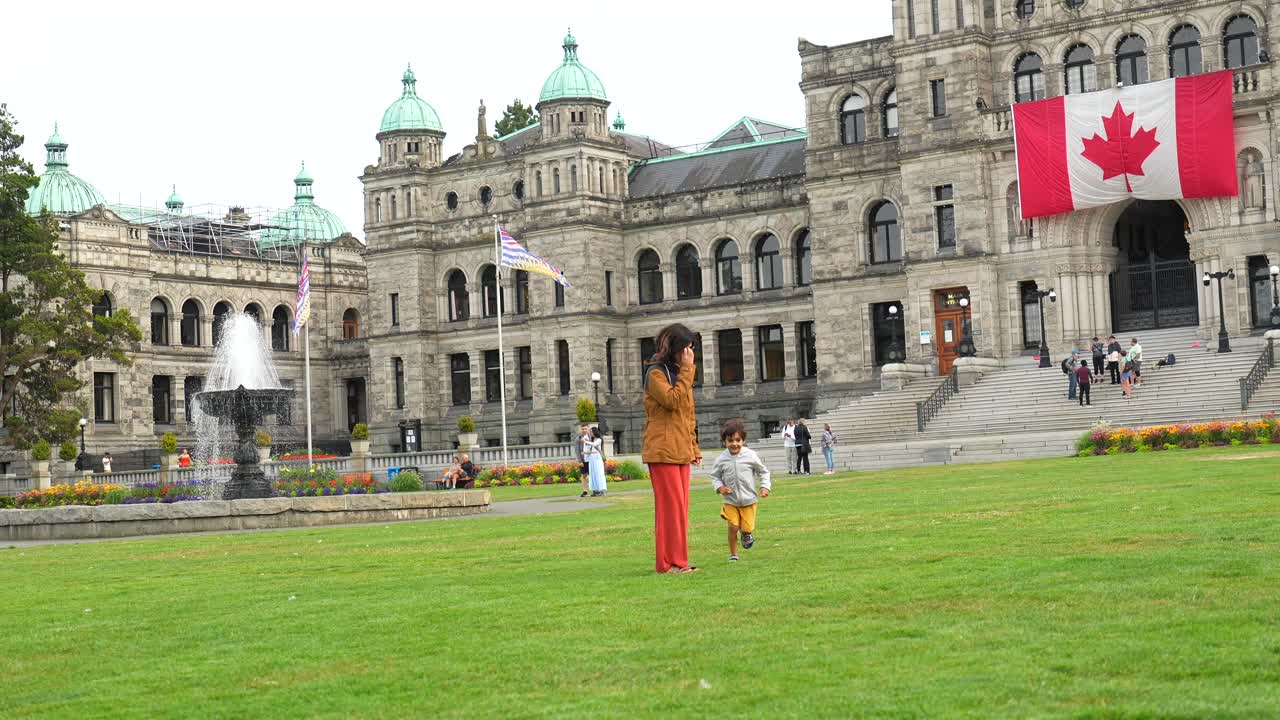 Famiglia che corre sul prato di fronte al Palazzo del Parlamento a Victoria, Canada