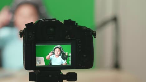 camera display of asian little boy holding mobile phone and talking to camera while live stream on green screen