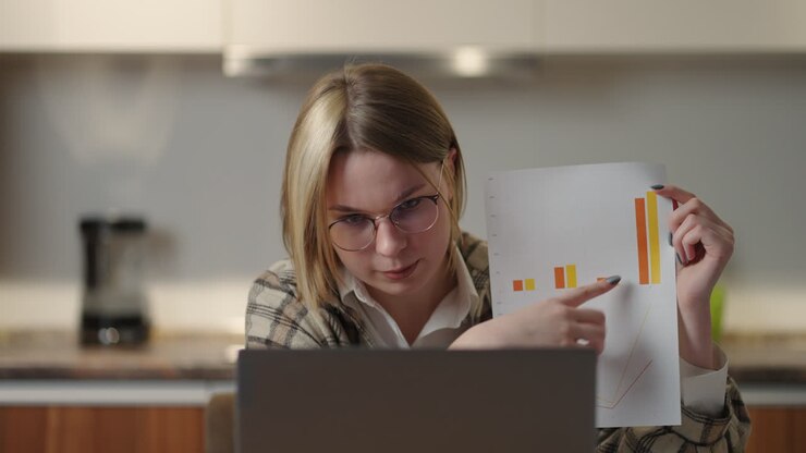 Ufficio domestico. Guardando la webcam, una giovane donna mostra un grafico alla telecamera e, gesticolando, mostra e spiega i valori dei dati e le analisi dell'azienda. Tesina.