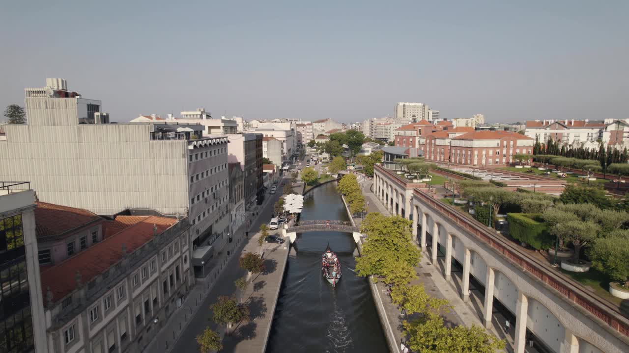 Ripresa aerea in discesa di una barca moliceiro che naviga su un canale d'acqua sotto un ponte pedonale.