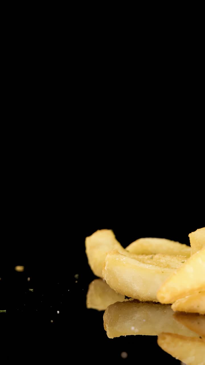 Golden French fries rotate on a reflective black surface under studio lighting, highlighting texture, seasoning, and crispness with smooth camera motion and dramatic mood