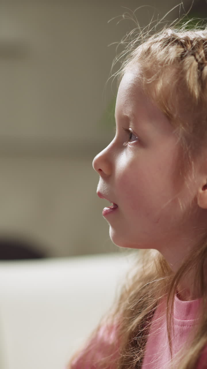 Pretty little girl with plaits answers test questions sitting with brother on sofa at homeschooling lesson in living room close side view slow motion