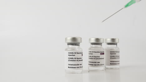 syringe needle pointing at covid-19 vaccine vials. static, white background