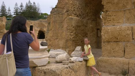 young mother doing photo on mobile phone to daughter in ruined carthage tunisia