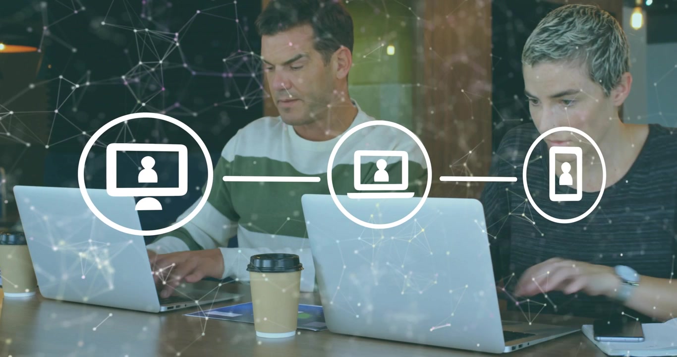 Uomo che digita su laptop, con overlay tecnologico trasparente che si espande e collega dispositivi mentre un collega digita
