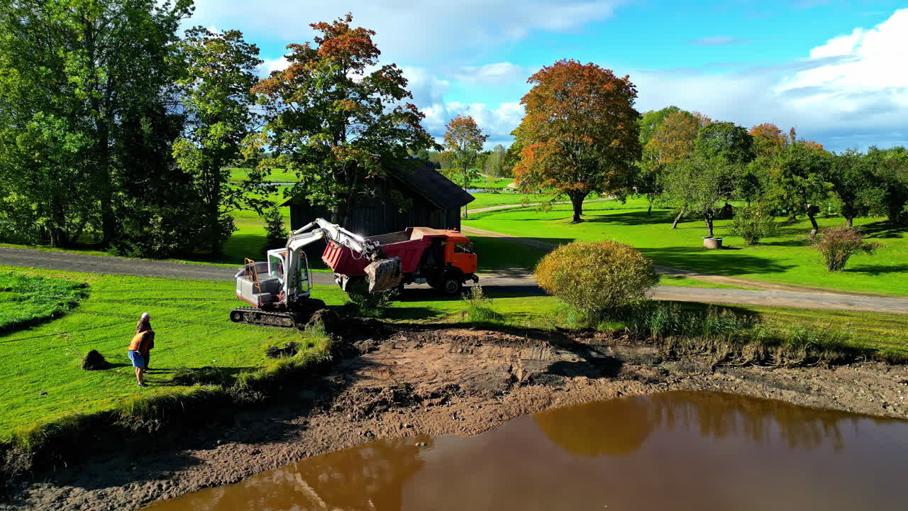 Excavator At Work Digging And Loading Soil Into Dump Truck For Hauling. wide drone shot