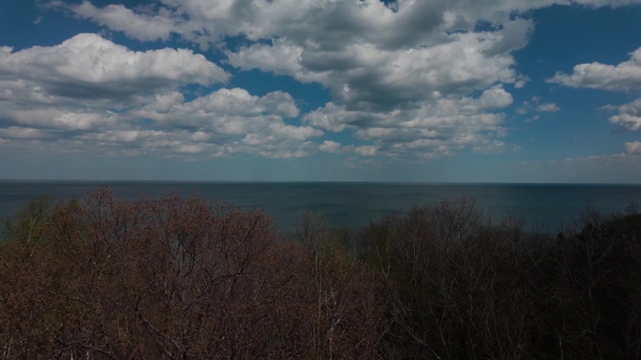 Panning down from clouds to a lake view and trees on the water.