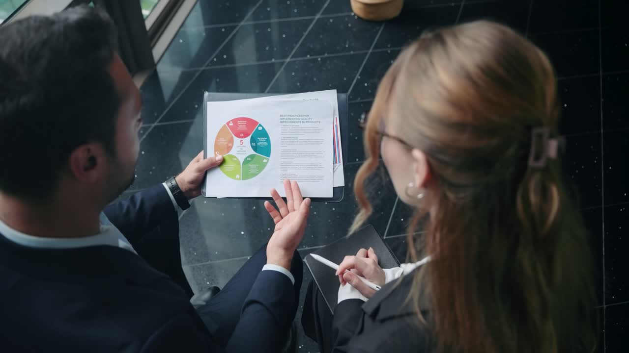 Imprenditrice che indica una sezione del grafico a torta con una penna, discutendo con il suo collega di analisi dei dati e strategia aziendale. - Scatto ad angolo elevato