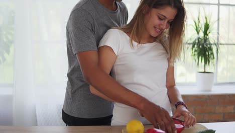 Attractive-african-man-is-embracing-his-caucasian-girlfriend-while-helping-her-to-prepare-food-in-the-kitchen-in-the-morning