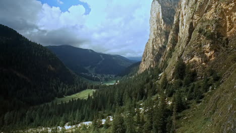 Green-valley-floor,-dark-green-spruce-trees,-a-spec-of-blue-sky-and-impressive-rock-walls