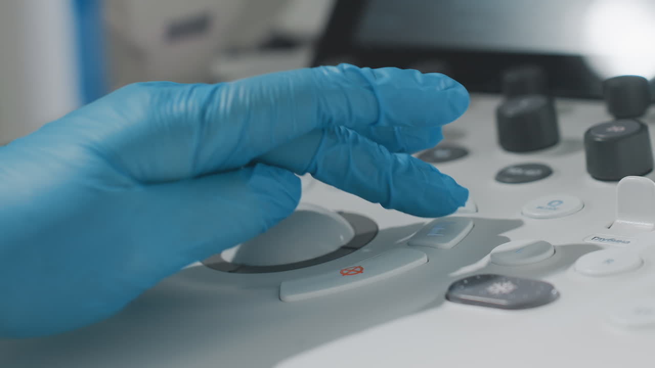 Close up of female clinical specialist wearing blue medical gloves operating scan equipment with precision during patient examination, adjusting buttons and controls on diagnostic interface