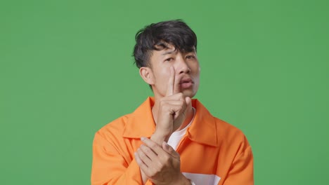 close up of asian male prisoner in handcuffs making shh gesture while standing on the green screen background