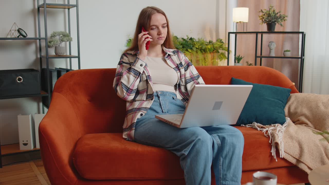 Young woman using laptop computer sitting on sofa working online shopping from home office