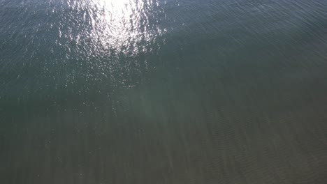 Stunning-iridescent-reflection-of-sun-in-deep-sea-water,-oceanside-offshore-drone