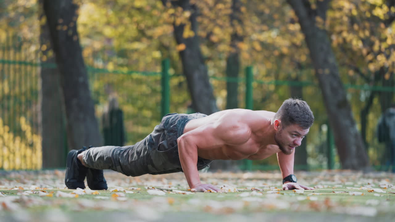Muscular athlete doing push-ups outside. Sporty guy is training in nature. Bearded male athlete exercising push-up on the stadium in autumn. Healthy lifestyle concept.
