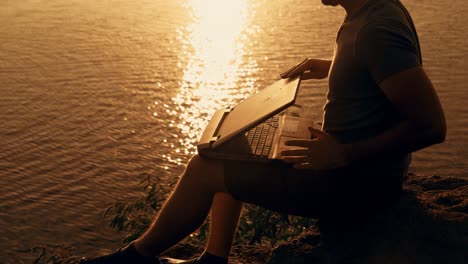 Young business man working on laptop at sunset. Freelance job online, focus on the screen