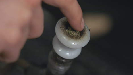 marijuana is pushed into a white bong bowl by a finger