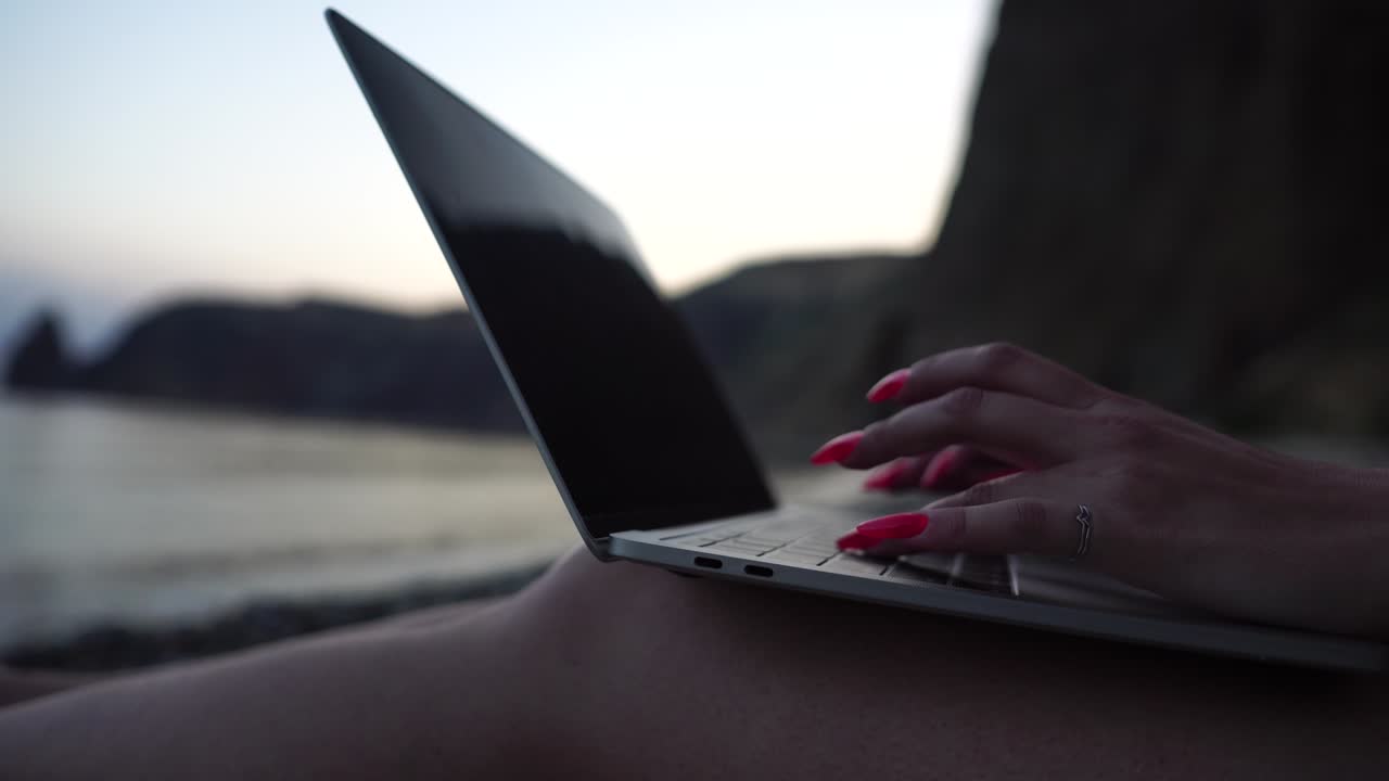 mujer de negocios exitosa con manicura roja brillante escribiendo en el teclado de la computadora portátil al aire libre en la playa con vista al mar. cerca de las manos de la mujer escribiendo en la computadora. freelance, nómada digital, viajes y vacaciones