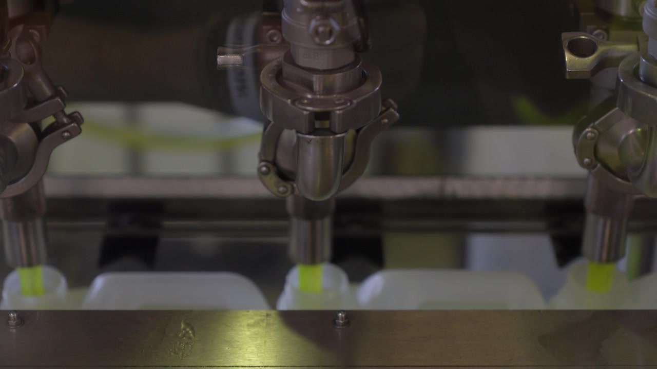 Automated bottling process of neon yellow coolant liquid into white canisters through hoses. Industrial production in a chemical factory plant.