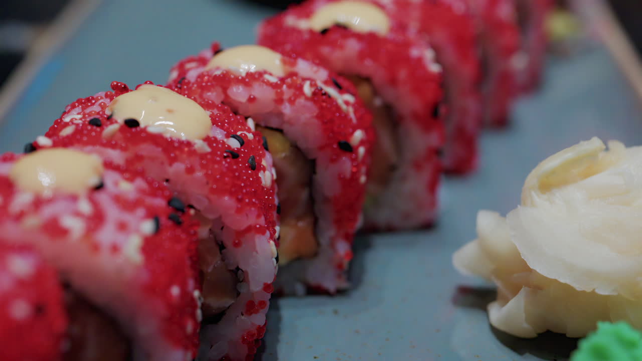 Close up of vibrant red sushi rolls topped with creamy sauce and sesame seeds, served on a ceramic plate