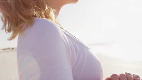 mujer caucásica sosteniendo un tapete deportivo en la playa y el fondo del cielo azul