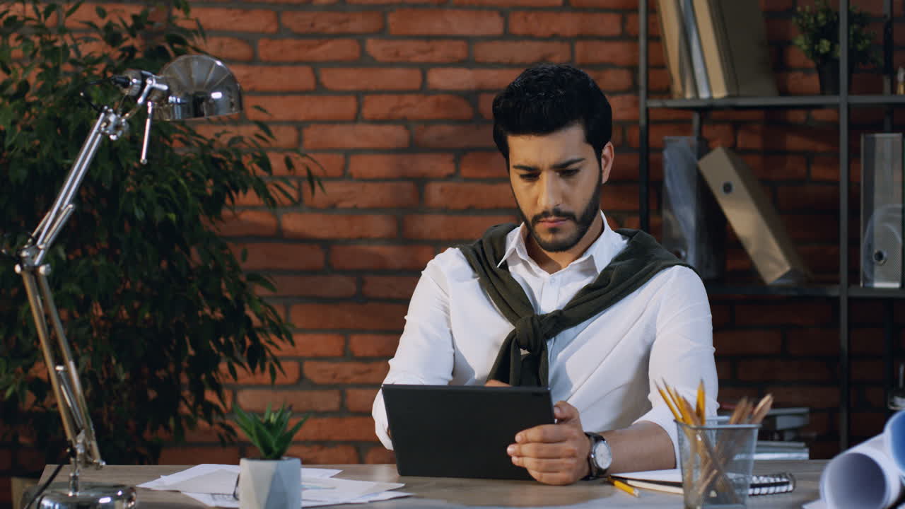 Young Arabian Businessman Scrolling And Taping On The Tablet While Sitting In The Modern Office