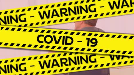 Words-Warning-Covid-19-written-on-yellow-tape-over-a-senior-man--in-background.-Covid-19-spreading