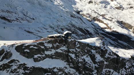 Aerial-panning-shot:-rocky-facade-in-the-Swiss-alps,-stones-and-snow-plains