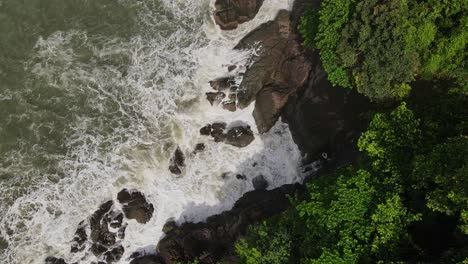 Vista-Aérea-De-Alto-ángulo-Sobre-Las-Islas-Exóticas-Copas-De-Los-árboles-Moviéndose-Hacia-La-Marea-Oceánica-Salpicada-Contra-La-Costa-Rocosa