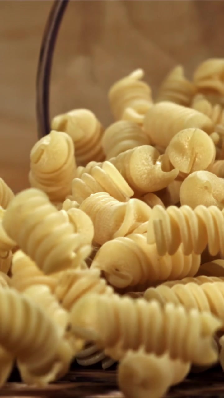 Dry Spiral Pasta Pouring from a Glass Bowl onto a Wooden Surface