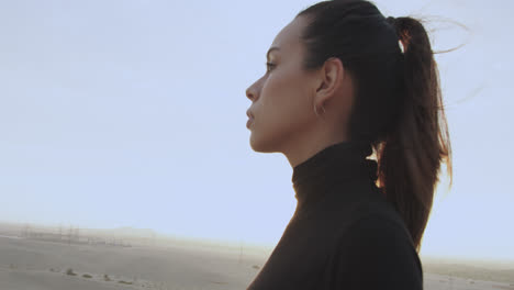 mujer de lado parada en medio del desierto al atardecer a la luz del sol poniente