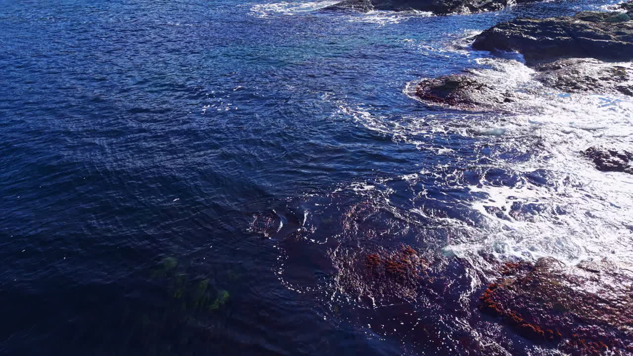 Waves crashing against rocky shore under bright sunlight at a serene coastal escape