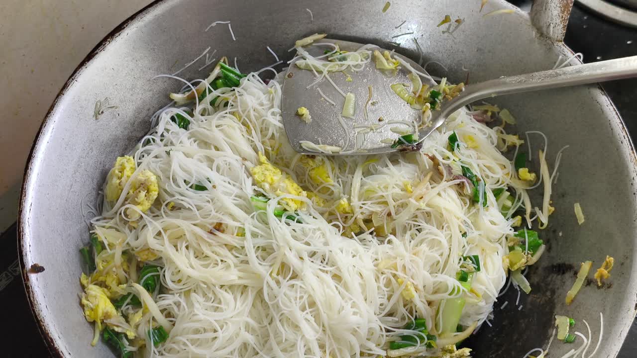 Chef is frying bihun (rice vermicelli) mixed with vegetables, egg, and spices. This flavourful dish is a popular Malaysian food, often served as a quick meal