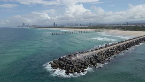 sand bypass pumping jetty - waves crashing on the spit gold coast with boats cruising at nerang river in gold coast, qld, australia