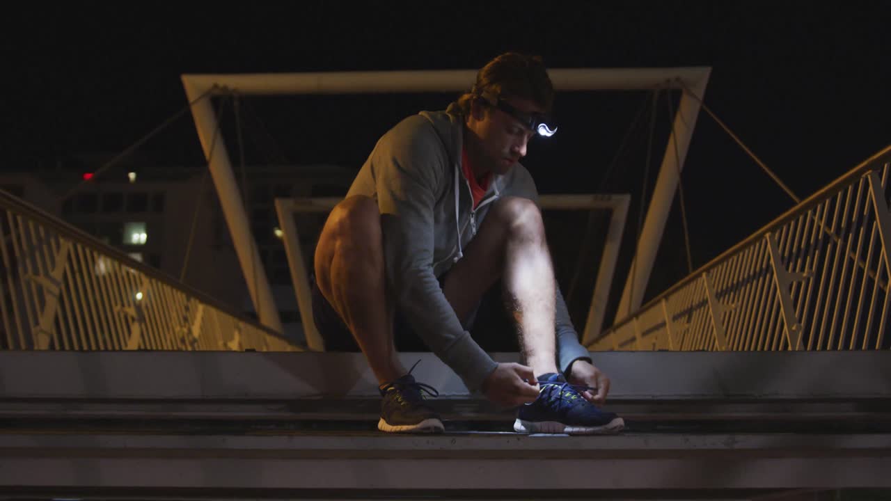 Caucasian male wearing a headlamp and tying his lacet on stairs in the evening